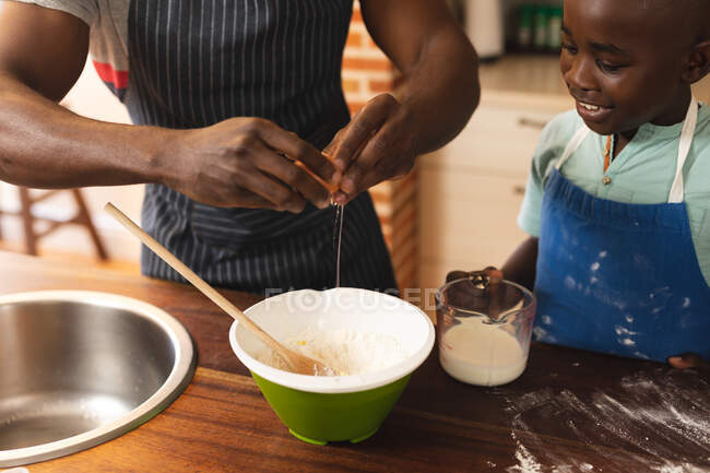 Mittlerer Abschnitt der afrikanisch-amerikanischen Vater und Sohn mit Schürzen backen in der Küche zu Hause. Weihnachtsfest Tradition Feier Konzept — Stockfoto