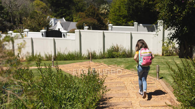 Chica caucásica con el pelo corto y oscuro caminando a la escuela llevando la mochila. educación y estilo de vida durante la pandemia de coronavirus covid 19 - foto de stock