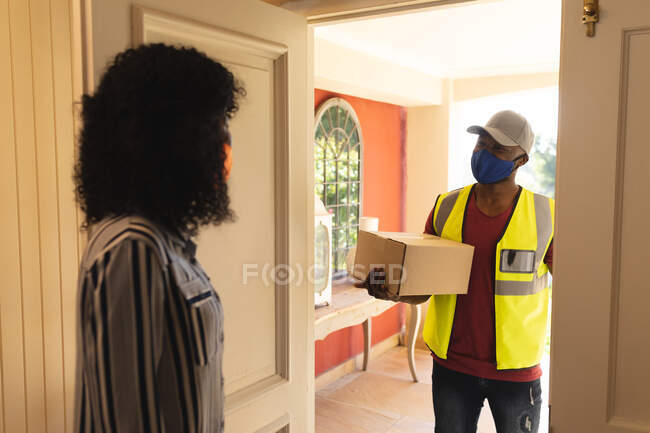 Delivery man wearing face mask delivering package to woman wearing face mask at home. social distancing during covid 19 coronavirus quarantine lockdown — Stock Photo