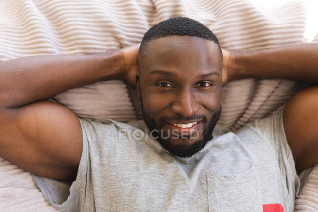 Retrato do homem afro-americano sorrindo deitado com as mãos atrás da cabeça em casa. Natal festa tradição celebração conceito — Fotografia de Stock