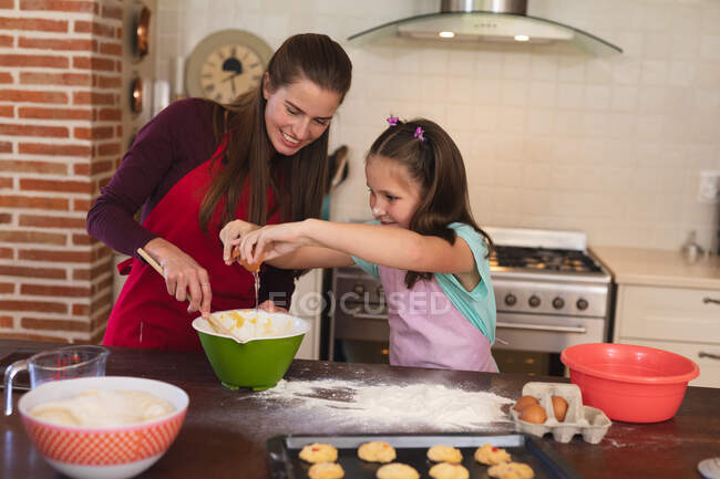 Caucasian woman with her daughter baking in a kitchen and wearing aprons. self isolation at home during coronavirus covid 19 quarantine lockdown. — Stock Photo