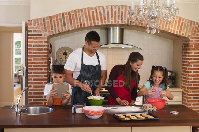 Kaukasische Familie backt in der Küche und trägt Schürzen, lächelt und verwendet Tabletten. qualitativ hochwertiger Lebensstil Familienzeit zusammen. — Stockfoto