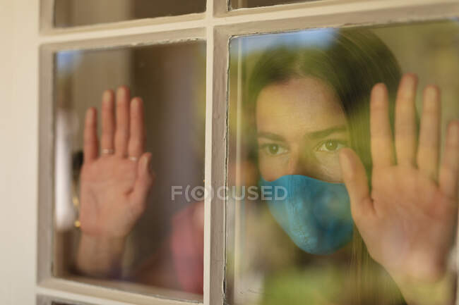 Kaukasische Frau, die aus dem Fenster schaut und Gesichtsmaske trägt. Selbstisolation zu Hause während Coronavirus covid 19 Quarantäne Lockdown. — Stockfoto