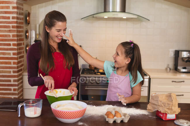 Femme caucasienne avec sa fille cuisinant dans une cuisine et portant des tabliers. isolement personnel à la maison pendant le confinement en quarantaine du coronavirus covid 19. — Photo de stock