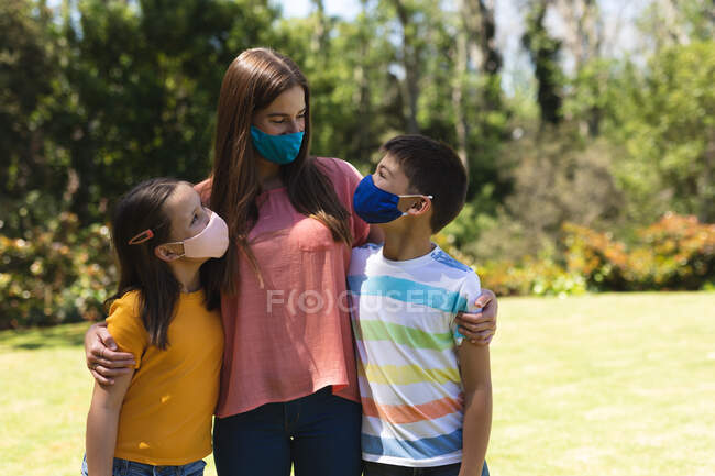 Donna caucasica e suo figlio e sua figlia indossano maschere facciali e si abbracciano all'aperto al sole. famiglia tempo di qualità insieme durante coronavirus covid 19 isolamento di quarantena. — Foto stock