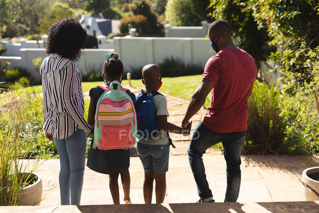 Rear view of african american family wearing face mask standing in the garden holding hands on a bright sunny day. social distancing during covid 19 coronavirus quarantine lockdown — Stock Photo