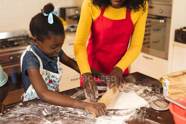 Madre e hija afroamericanas usando delantal horneando en la cocina en casa. fiesta de navidad tradición celebración concepto - foto de stock