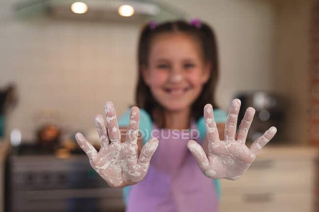 Porträt eines kaukasischen Mädchens in einer Küche, das in die Kamera blickt und ihre Hände mit Mehl zeigt. Selbstisolation zu Hause während Coronavirus covid 19 Quarantäne Lockdown. — Stockfoto