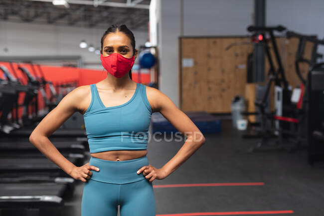Портрет белой женщины в маске, стоящей в спортзале. социальная изоляция от карантина во время пандемии коронавируса — стоковое фото