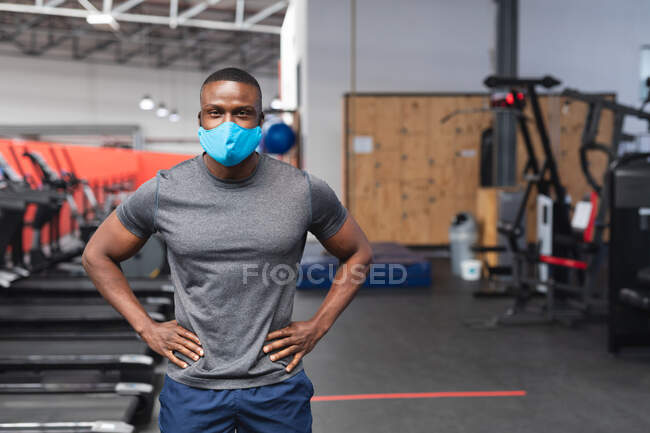 Портрет афроамериканського чоловіка, одягненого в маску обличчя, стоїть у спортзалі. Відстань до карантину під час пандемії коронавірусу — стокове фото