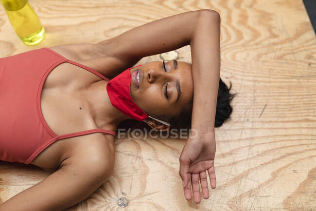 Fit  caucasian woman wearing face mask around her neck resting while lying on wooden plyo box in the gym. social distancing quarantine lockdown during coronavirus pandemic — Stock Photo