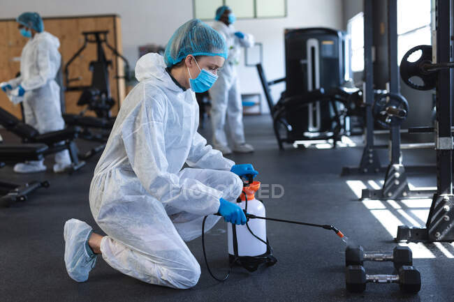 Arbeiterinnen mit Schutzkleidung und Mundschutz reinigen die Turnhalle mit Desinfektionsmittel. Soziale Distanzierung von Quarantäne während der Coronavirus-Pandemie — Stockfoto