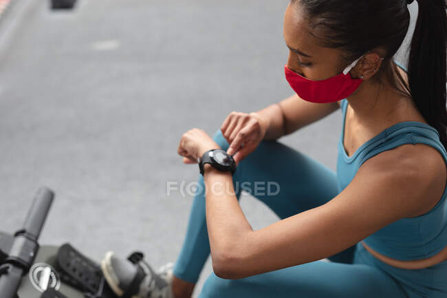 Fit femme caucasienne portant un masque facial en utilisant smartwatch dans la salle de gym. isolement social mise en quarantaine pendant une pandémie de coronavirus — Photo de stock