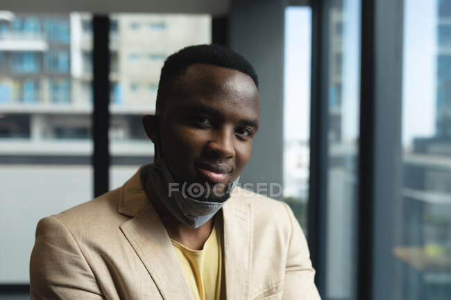 Retrato del hombre afroamericano sonriendo en la oficina moderna. distanciamiento social bloqueo de cuarentena durante la pandemia de coronavirus - foto de stock