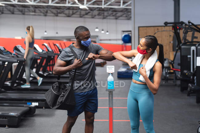 Ajuste hombre afroamericano y ajuste mujer caucásica saludándose entre sí tocando los codos en el gimnasio. distanciamiento social bloqueo de cuarentena durante la pandemia de coronavirus - foto de stock
