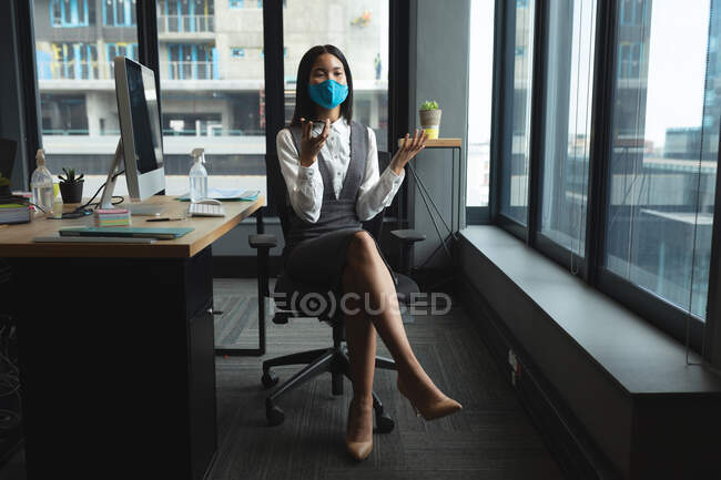 Asiatin mit Gesichtsmaske sitzt auf ihrem Schreibtisch im modernen Büro. Soziale Distanzierung von Quarantäne während der Coronavirus-Pandemie — Stockfoto