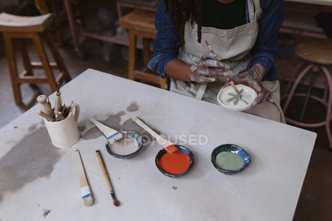 Female potter working in pottery studio. working at a working table, painting a plate. small creative business during covid 19 coronavirus pandemic. — Stock Photo