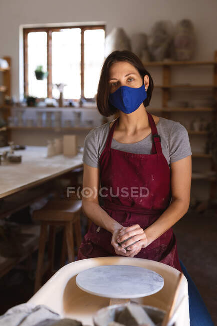 Porträt einer kaukasischen Frau mit Gesichtsmaske im Töpferatelier. kleine kreative Unternehmen während covid 19 Coronavirus-Pandemie. — Stockfoto