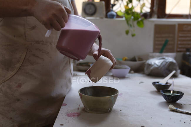 Female potter working in pottery studio. working at a potters wheel, painting a bowl. small creative business during covid 19 coronavirus pandemic. — Stock Photo
