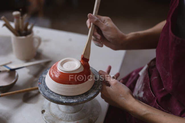 Potier féminin travaillant dans un atelier de poterie. travailler à une roue de potiers, peindre un bol. petite entreprise créative pendant la pandémie de coronavirus covid 19. — Photo de stock