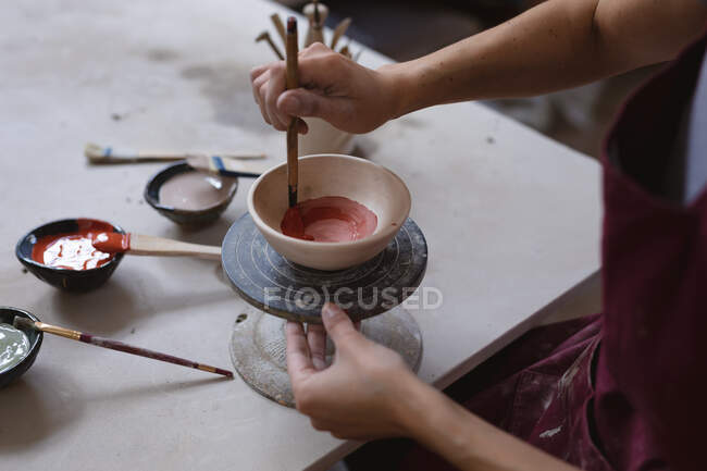 Female potter working in pottery studio. working at a potters wheel, painting a bowl. small creative business during covid 19 coronavirus pandemic. — Stock Photo