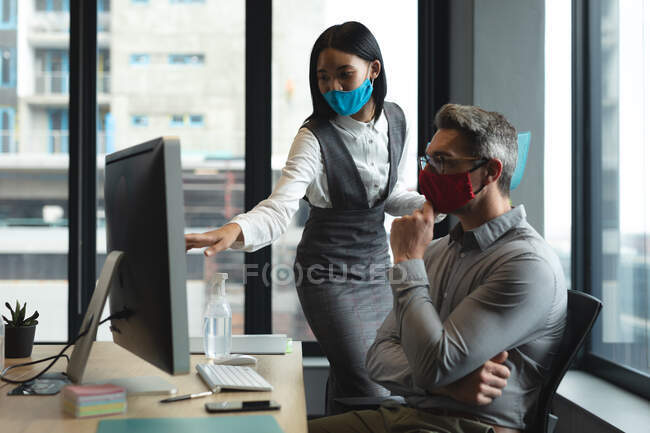 Кавказький чоловік і жінка в масках обличчя працюють разом у сучасному офісі. Відстань до карантину під час пандемії коронавірусу — стокове фото