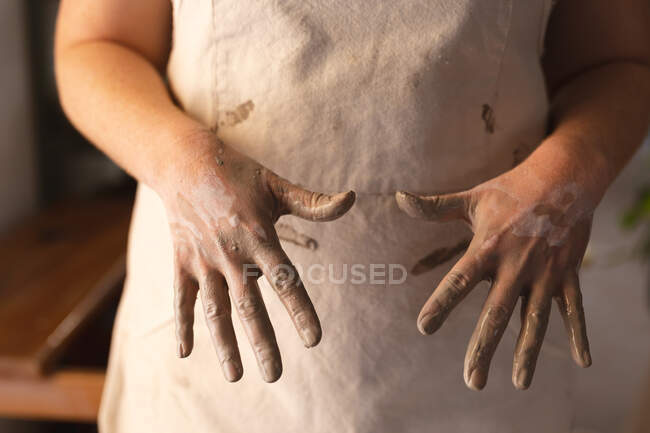 Töpferin arbeitet im Töpferatelier. zeigt ihre schmutzigen Hände in die Kamera. kleine kreative Unternehmen während covid 19 Coronavirus-Pandemie. — Stockfoto