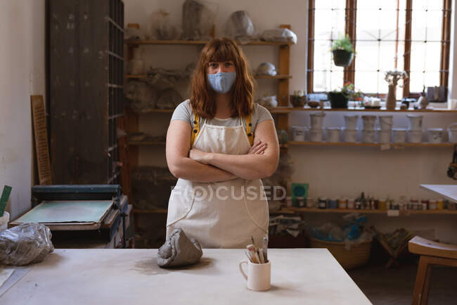 Ritratto di donna caucasica con maschera facciale allo studio di ceramica. piccola attività creativa durante covid 19 coronavirus pandemia. — Foto stock