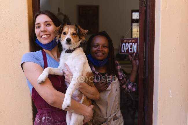 Portrait of caucasian and mixed race women at pottery studio, holding a puppy. small creative business during covid 19 coronavirus pandemic. — Stock Photo