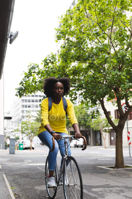 African american woman riding on bicycle on a street out and about in the city during covid 19 coronavirus pandemic. — Stock Photo