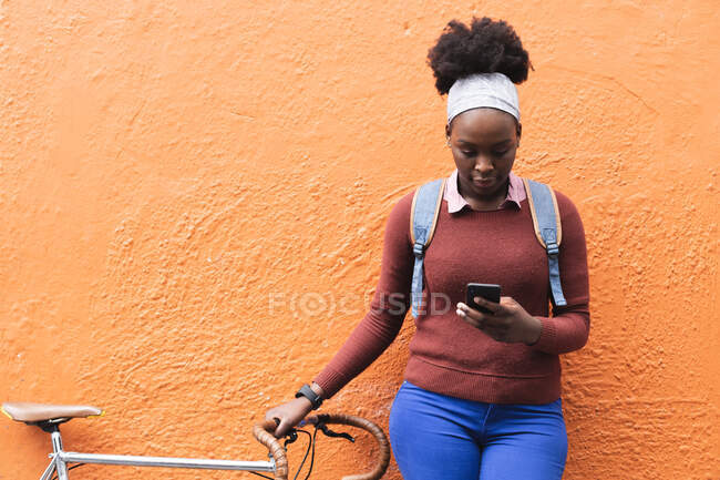 Retrato de mulher afro-americana usando smartphone na rua segurando sua bicicleta para fora e sobre na cidade durante a pandemia de coronavírus covid 19. — Fotografia de Stock