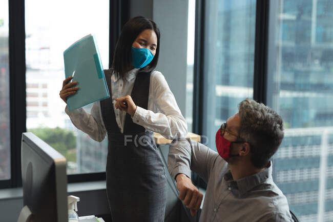 Diverse male and female colleagues wearing face masks touching elbows in office. hygiene and social distancing in the workplace during coronavirus covid 19 pandemic. — Stock Photo