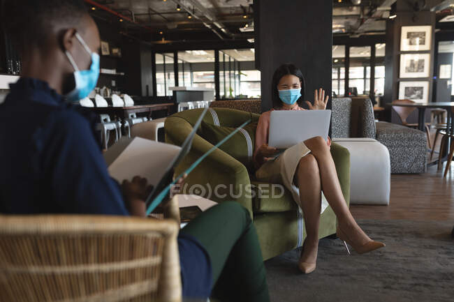 Азійка, одягнена в маску, має відеобесіду на ноутбуці в сучасному офісі. Відстань до карантину під час пандемії коронавірусу — стокове фото