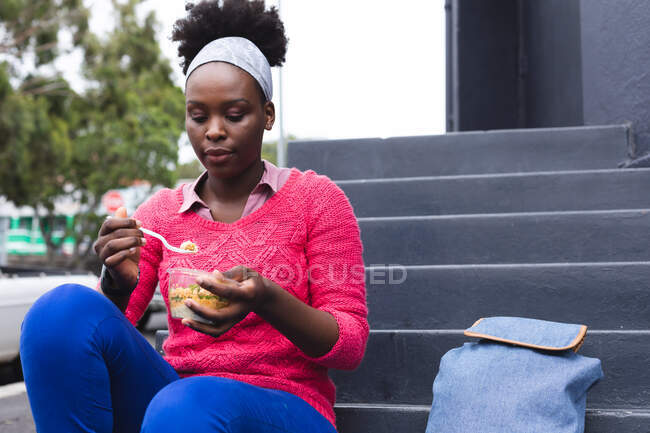 Mujer afroamericana comiendo una ensalada en la calle en la ciudad durante la pandemia de coronavirus covid 19. - foto de stock