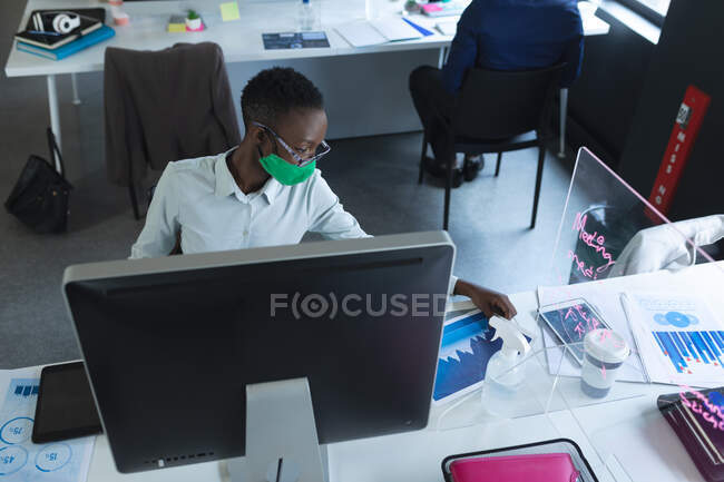 Donna afroamericana con maschera facciale che legge documenti in ufficio. isolamento di quarantena a distanza sociale durante la pandemia di coronavirus. — Foto stock