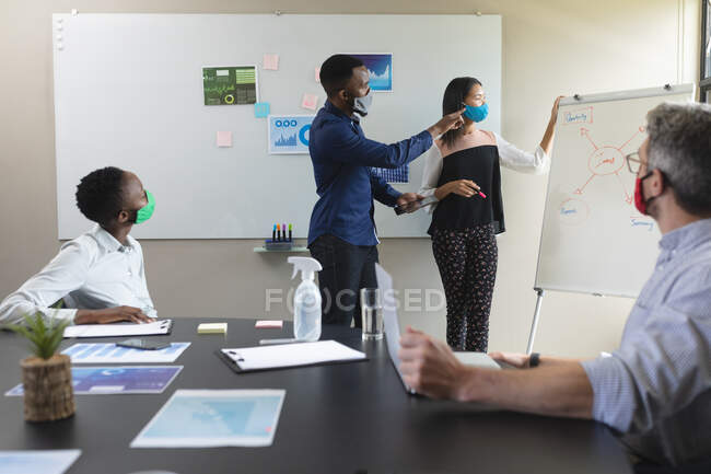 Diverse male and female colleagues wearing face masks giving presentation. social distancing quarantine lockdown during coronavirus pandemic. — Stock Photo