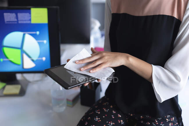 Mittelteil einer Frau, die im modernen Büro ein digitales Tablet mit Gewebe reinigt. Hygiene und soziale Distanzierung am Arbeitsplatz während der Coronavirus-Pandemie 19. — Stockfoto