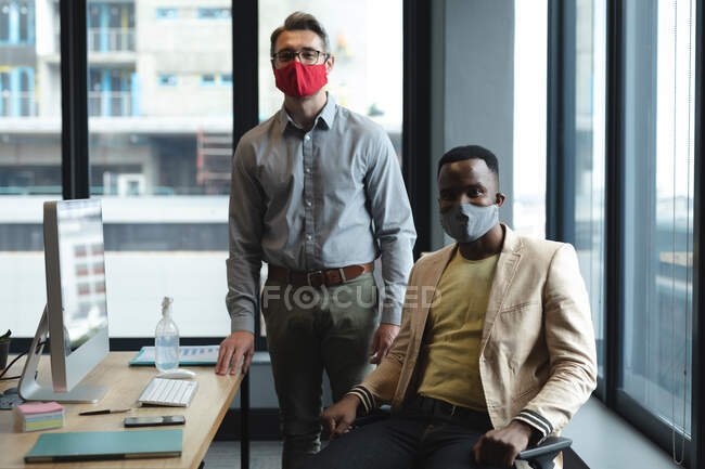 Retrato de diversos colegas masculinos que usan máscaras faciales en la oficina moderna. distanciamiento social bloqueo de cuarentena durante la pandemia de coronavirus - foto de stock