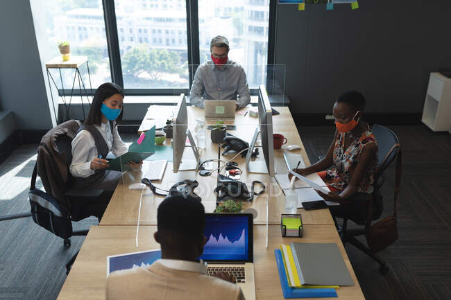 Diverse colleagues wearing face masks at office. working on computers sitting at their desks. hygiene and social distancing in the workplace during coronavirus covid 19 pandemic. — Stock Photo