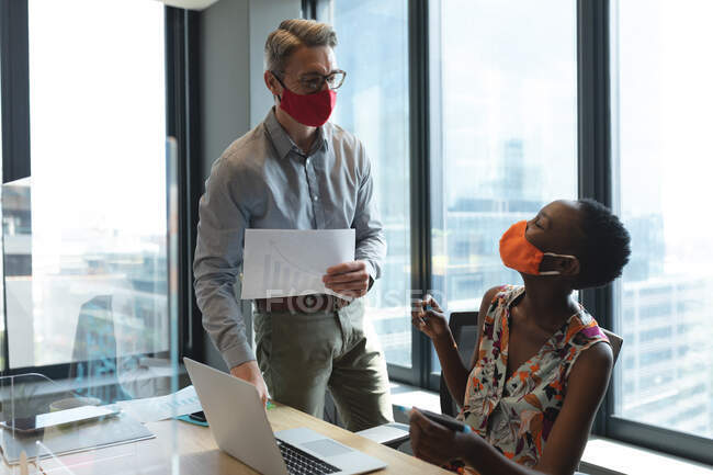 Diversos colegas masculinos y femeninos con máscaras faciales que hablan entre sí en la oficina moderna. distanciamiento social bloqueo de cuarentena durante la pandemia de coronavirus - foto de stock