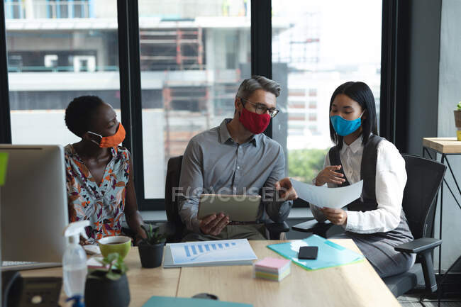 Diversos colegas que usan máscaras faciales trabajando juntos en la oficina moderna. higiene y distanciamiento social en el lugar de trabajo durante la pandemia de coronavirus covid 19. - foto de stock