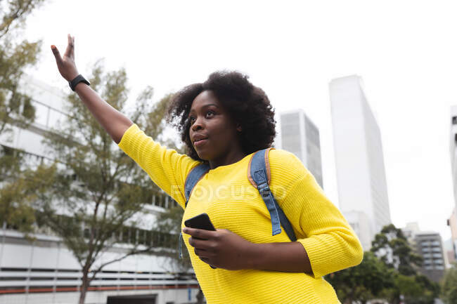 Afroamerikanerin mit Smartphone auf der Straße hebt während der 19. Coronavirus-Pandemie in der Stadt die Hand. — Stockfoto