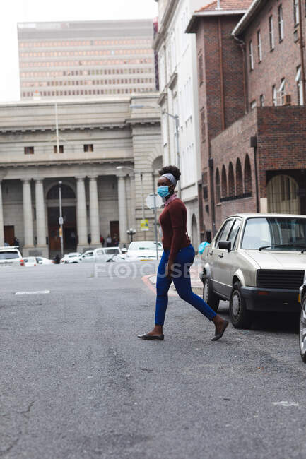 Femme afro-américaine portant un masque facial marchant dans la rue et dans la ville pendant la pandémie de coronavirus covid 19. — Photo de stock