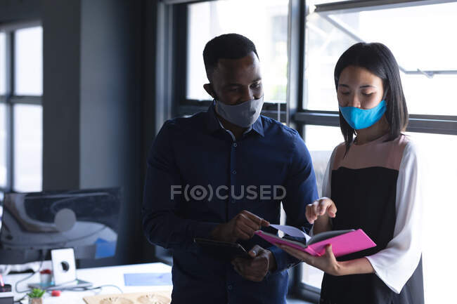 Diversos colegas masculinos e femininos usando máscaras faciais lendo um livro no escritório moderno. bloqueio de quarentena por distanciamento social durante a pandemia do coronavírus — Fotografia de Stock