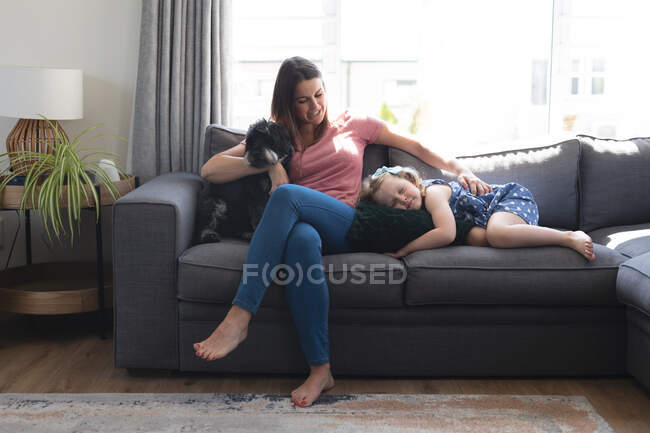Madre e hija caucásicas divirtiéndose tumbadas en el sofá. disfrutando de tiempo de calidad en casa durante coronavirus covid 19 pandemia de bloqueo. - foto de stock