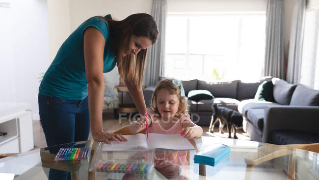 Madre e hija caucásicas divirtiéndose en la sala de estar dibujando en un cuaderno. disfrutando de tiempo de calidad en casa durante coronavirus covid 19 pandemia de bloqueo. - foto de stock