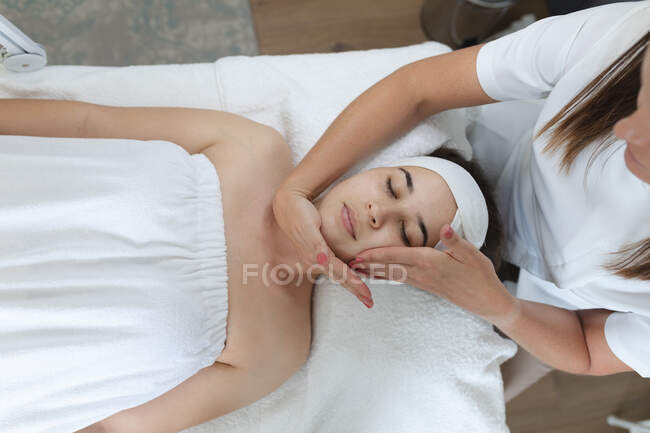 Femme blanche allongée tandis que l'esthéticienne lui donne un visage. client bénéficiant d'un traitement dans un salon de beauté. — Photo de stock