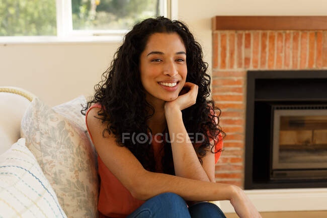 Portrait of mixed race woman sitting on couch in living room. self isolation at home during covid 19 coronavirus pandemic. — Stock Photo