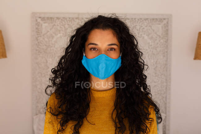 Retrato de mujer de raza mixta con pelo largo usando mascarilla. autoaislamiento en el hogar durante la pandemia de coronavirus covid 19. - foto de stock
