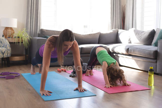 Кавказька мати і дочка практикують йогу в вітальні. Якісний час, проведений під час коронавірусного ув 